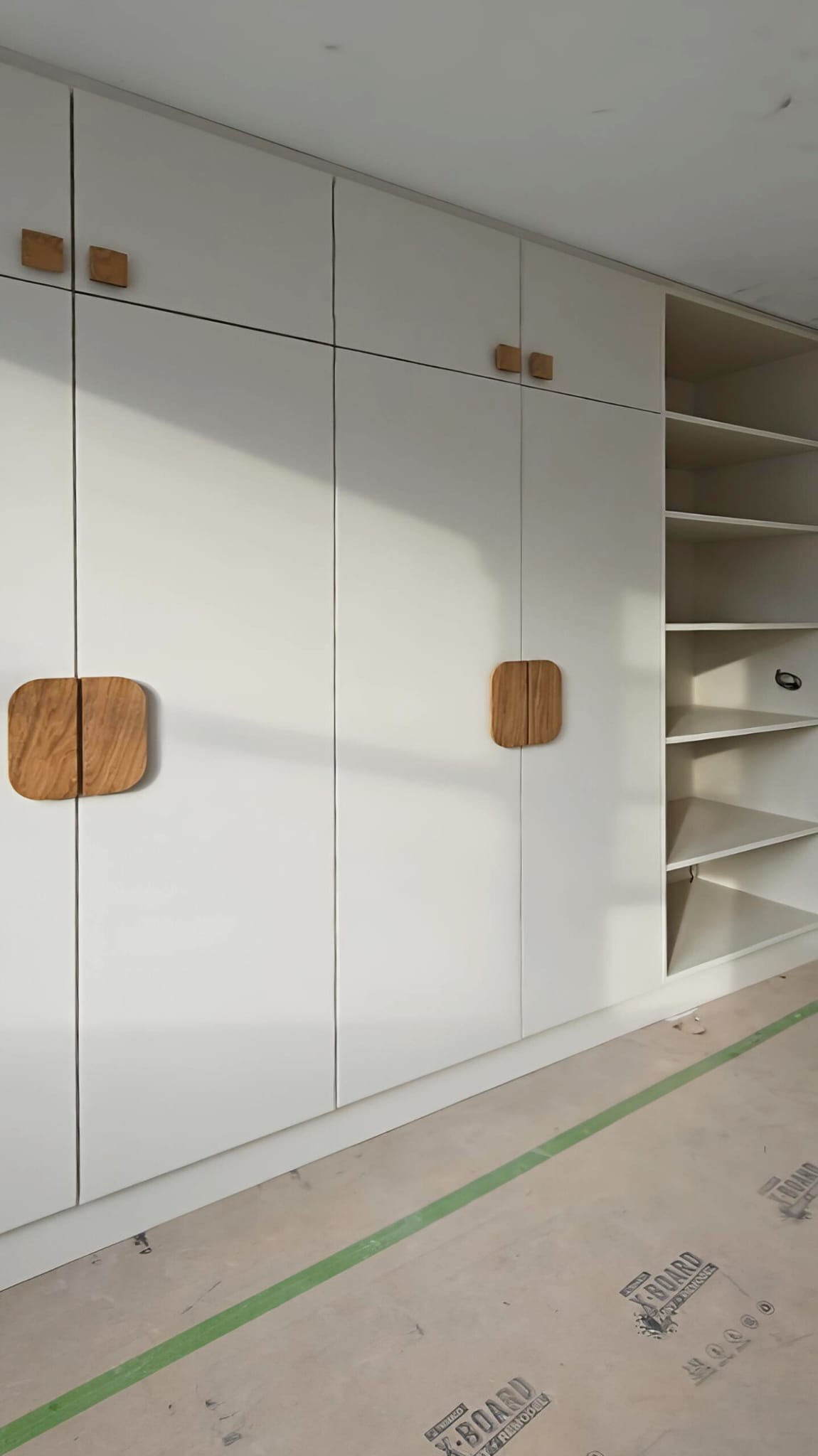 Wall-to-wall off-white fitted wardrobes and open bedroom shelving in Hackney