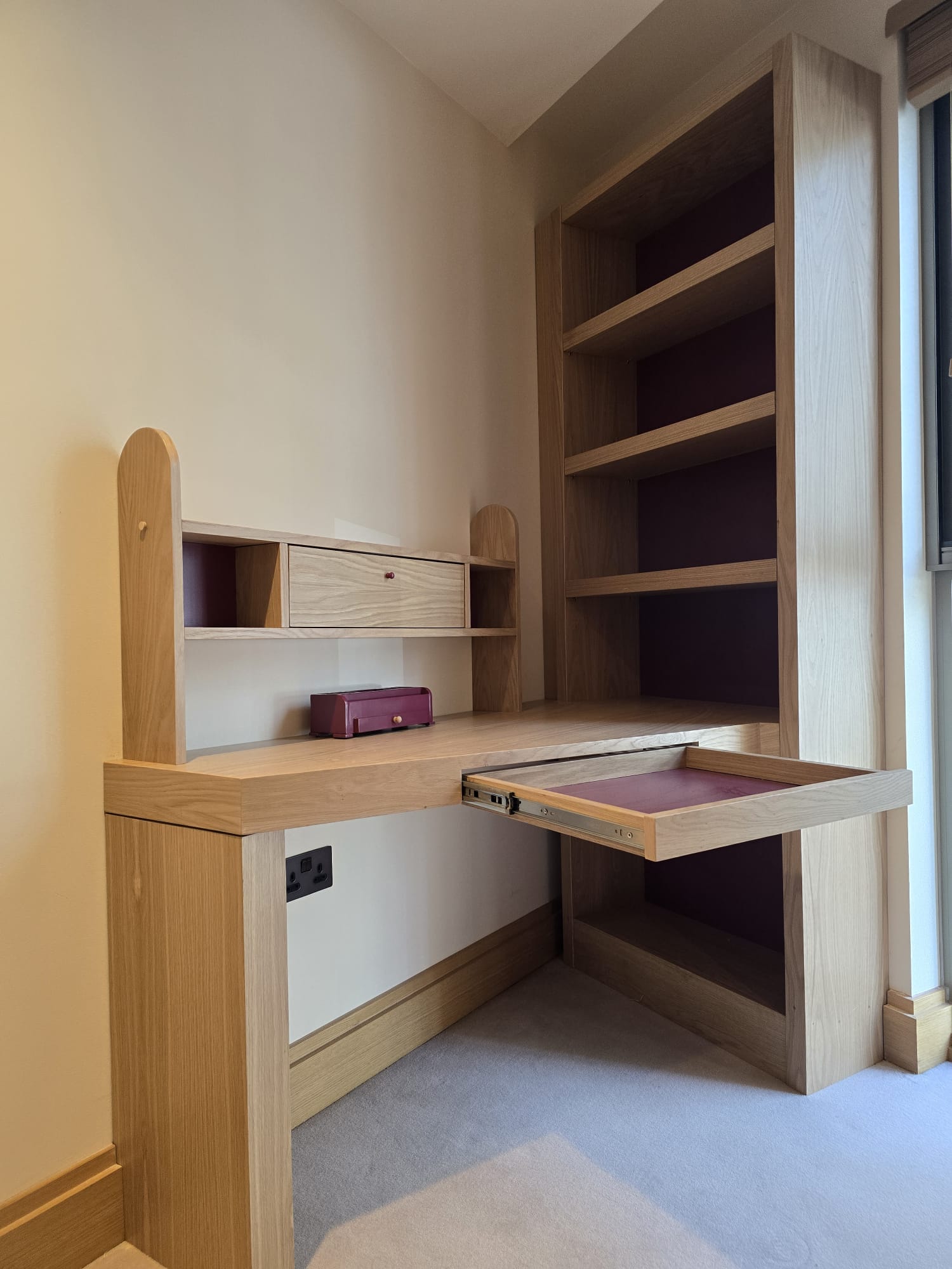 Shallow desk drawer with a purple interior beside an oak-veneered bookcase in Westminster