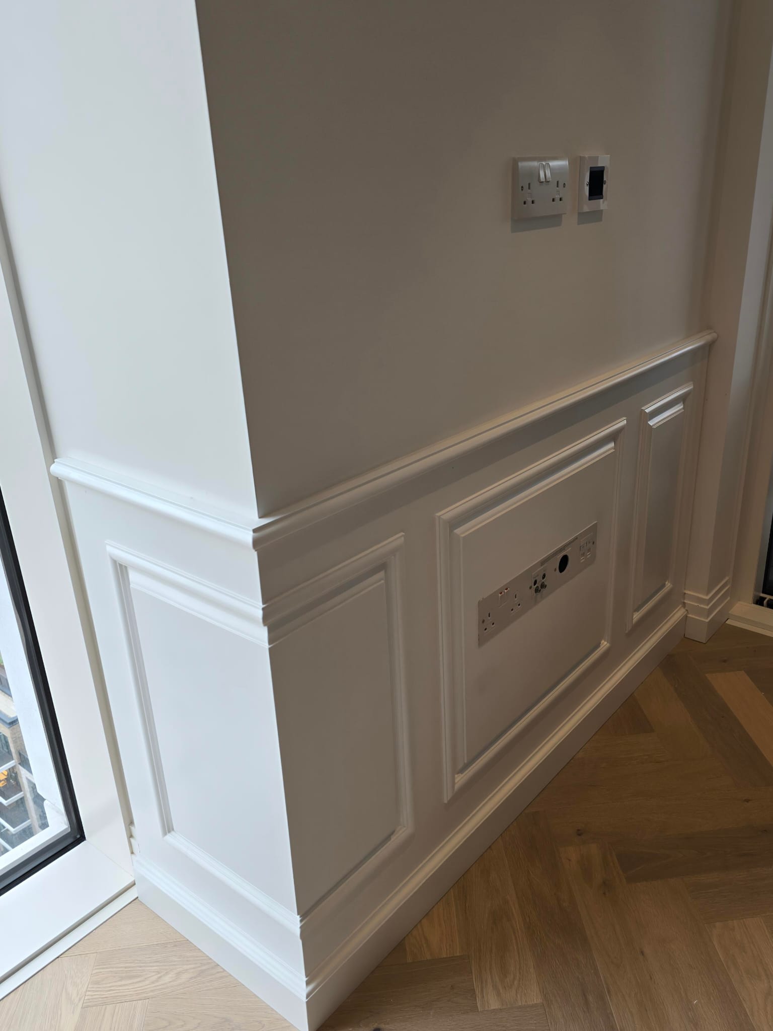 Lower wall panels and dado rail wrapping a corner beside a window in Chelsea