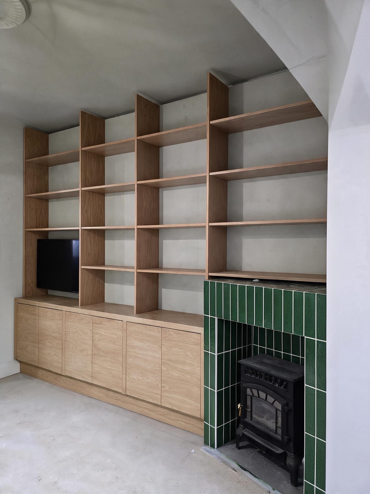 Bespoke wood-finish media wall with open shelving beside a green-tiled fireplace in Hackney, London