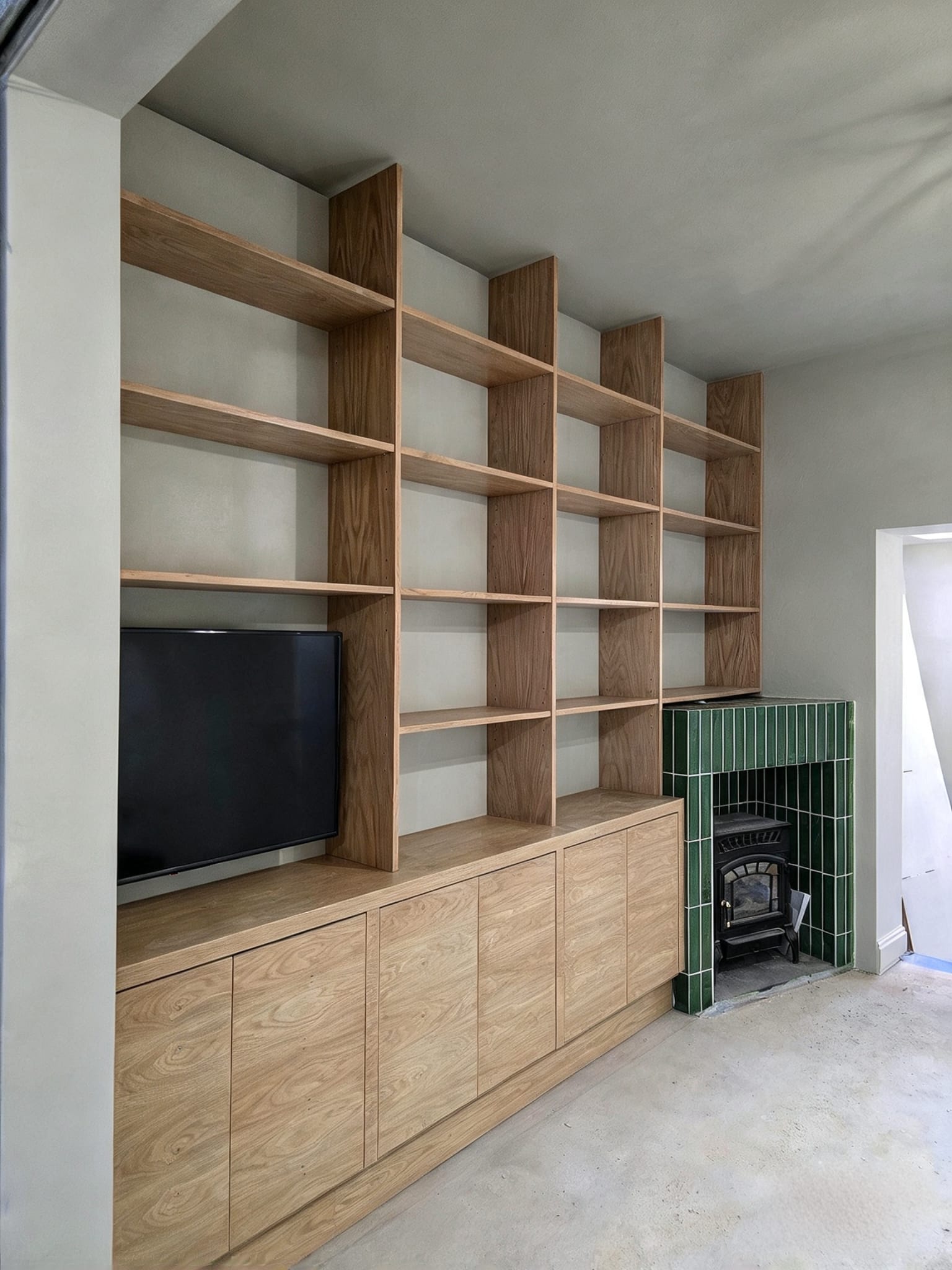 Fitted TV bay, full-height open shelves and handleless base cupboards in a Hackney living room