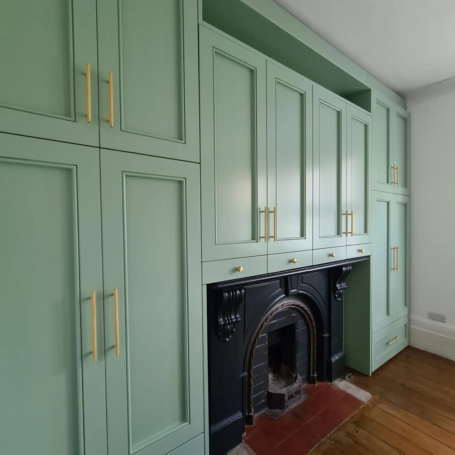 Sage green bespoke fitted wardrobes designed around a Victorian fireplace in Bromley, London
